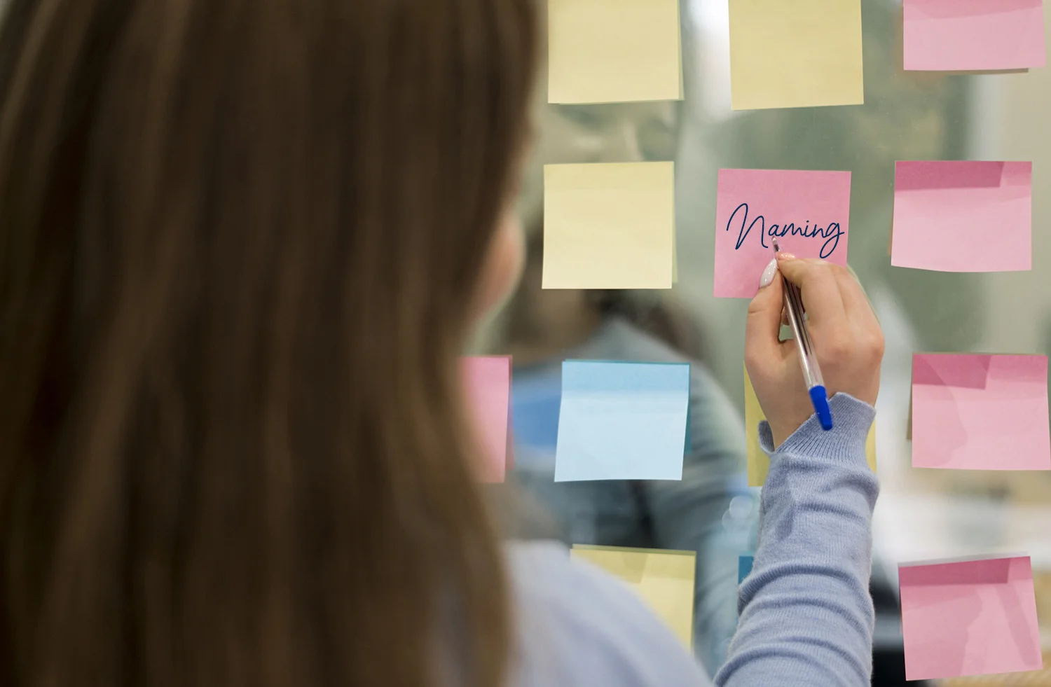 Mujer eccribiendo en un post its la palabra naming